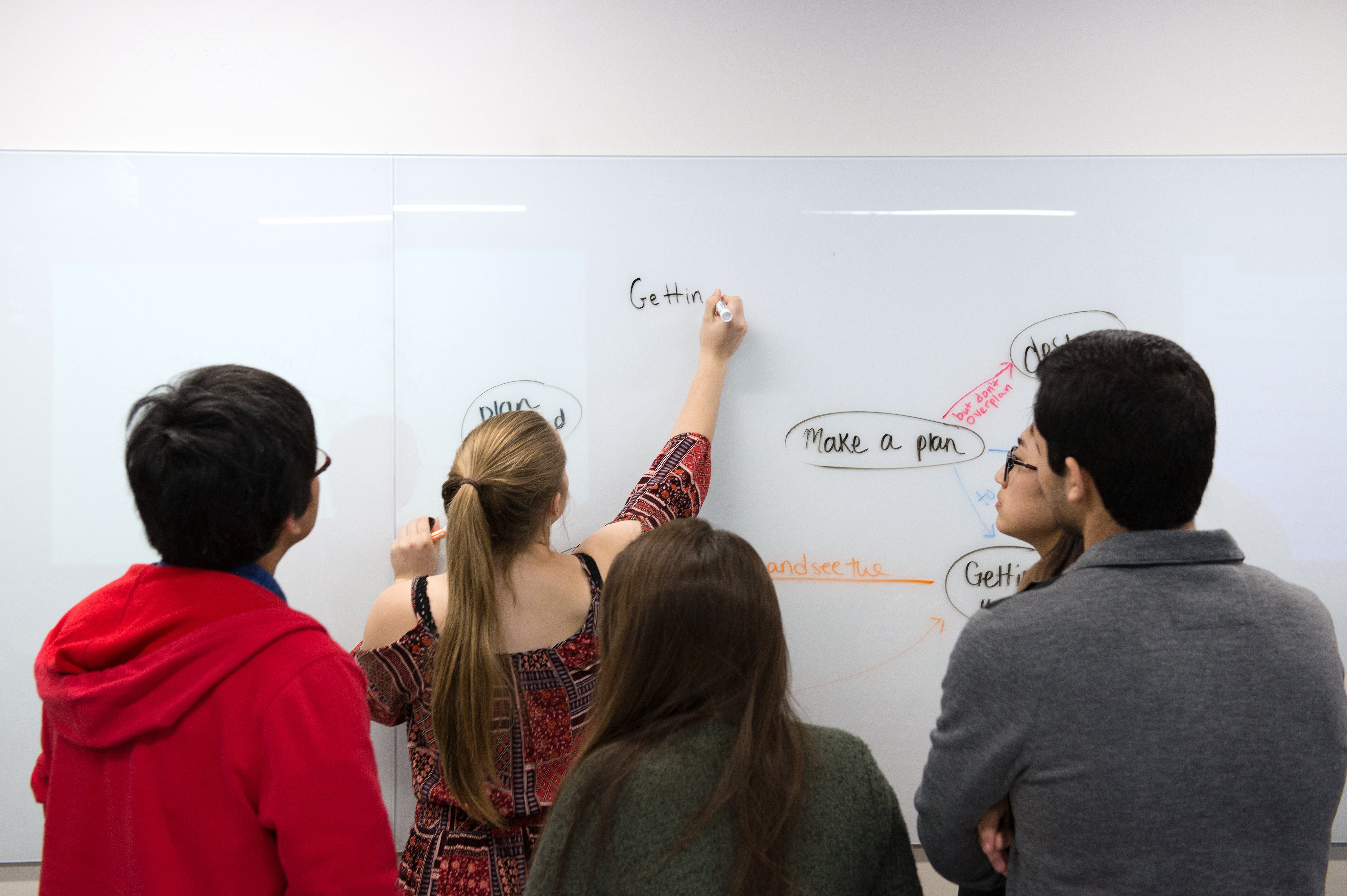 Four students writing words on a dry erase board.