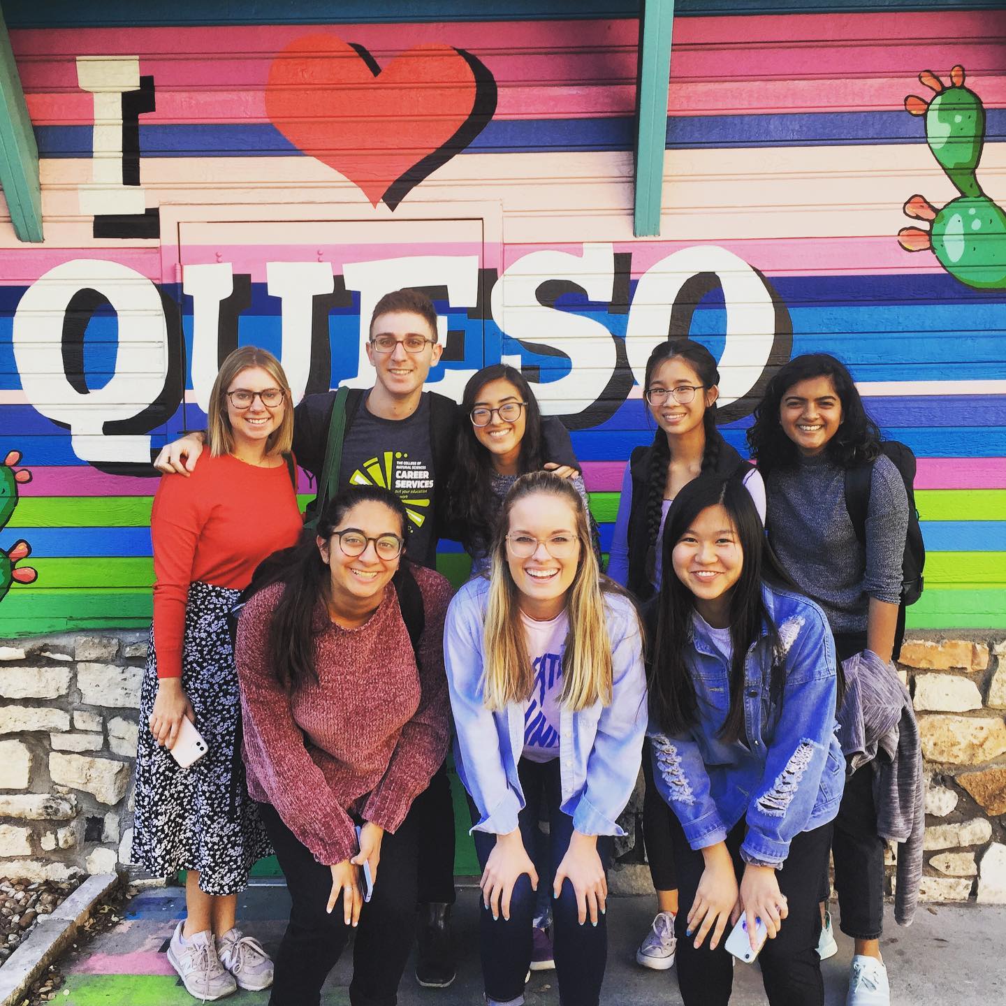 8 college students in front of "I love queso" mural